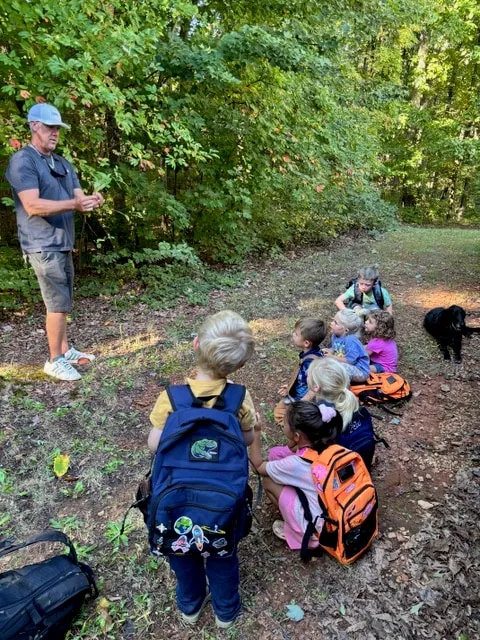 Teacher leading children on a nature walk at the edge of the woods