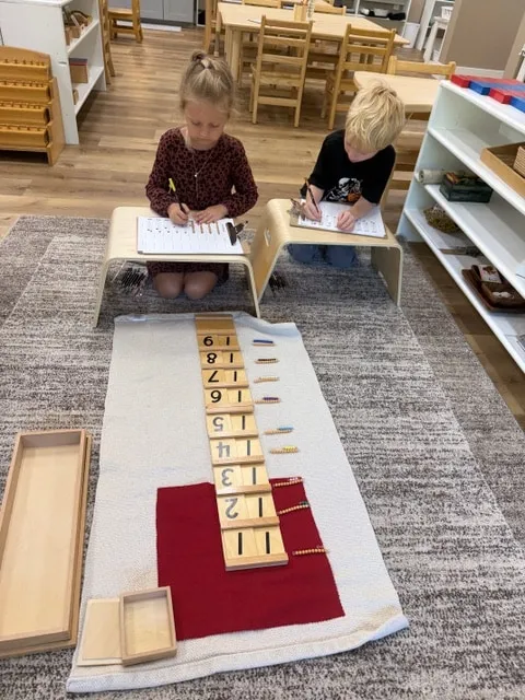 Two children working with bead materials and number cards on a classroom rug