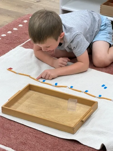Boy laying out a bead chain with number arrows on a floor mat