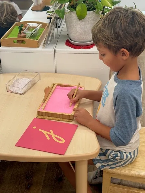 Boy tracing letters in a sand tray